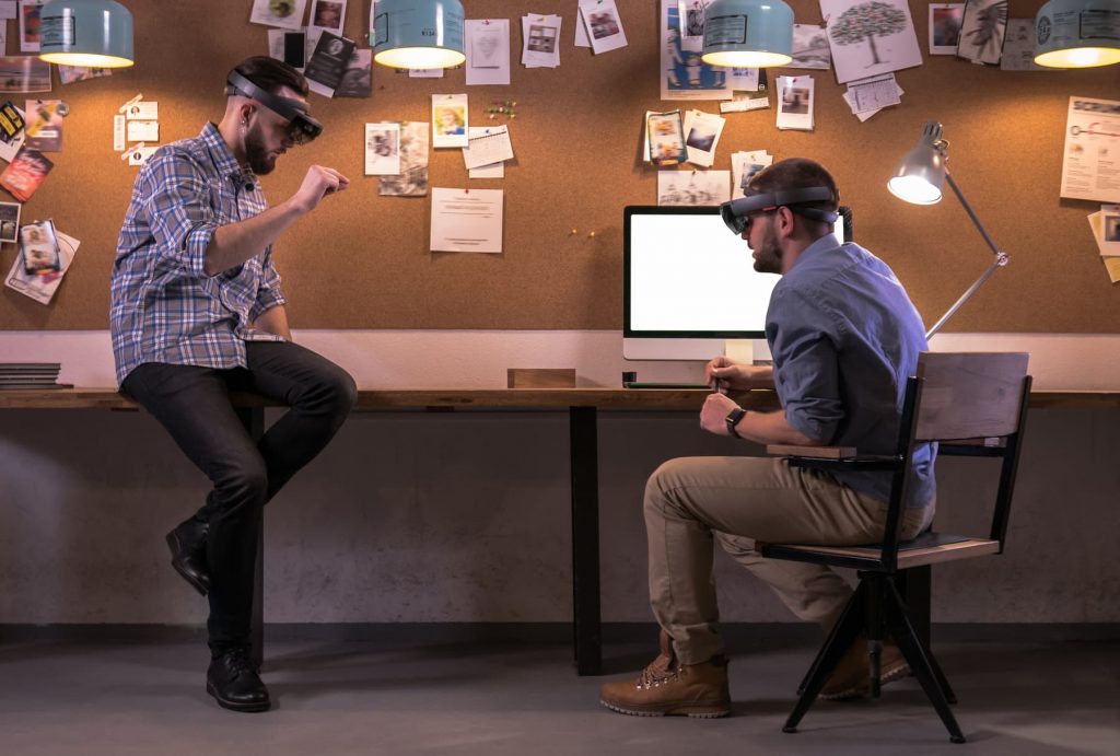 Hololens 2 - Two young adult Caucasian males discussing a project using holographic augmented reality glasses in trendy office