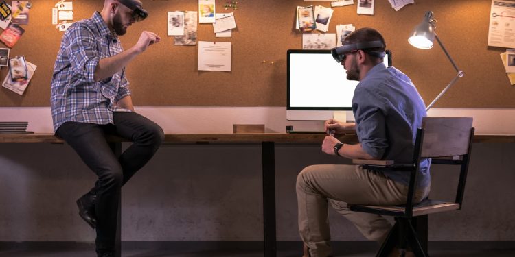 Hololens 2 - Two young adult Caucasian males discussing a project using holographic augmented reality glasses in trendy office